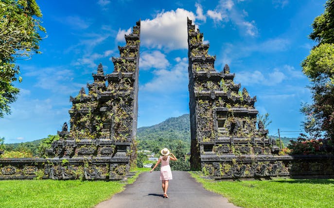 Person walking towards Bali Handara Gate with mountains in the background.