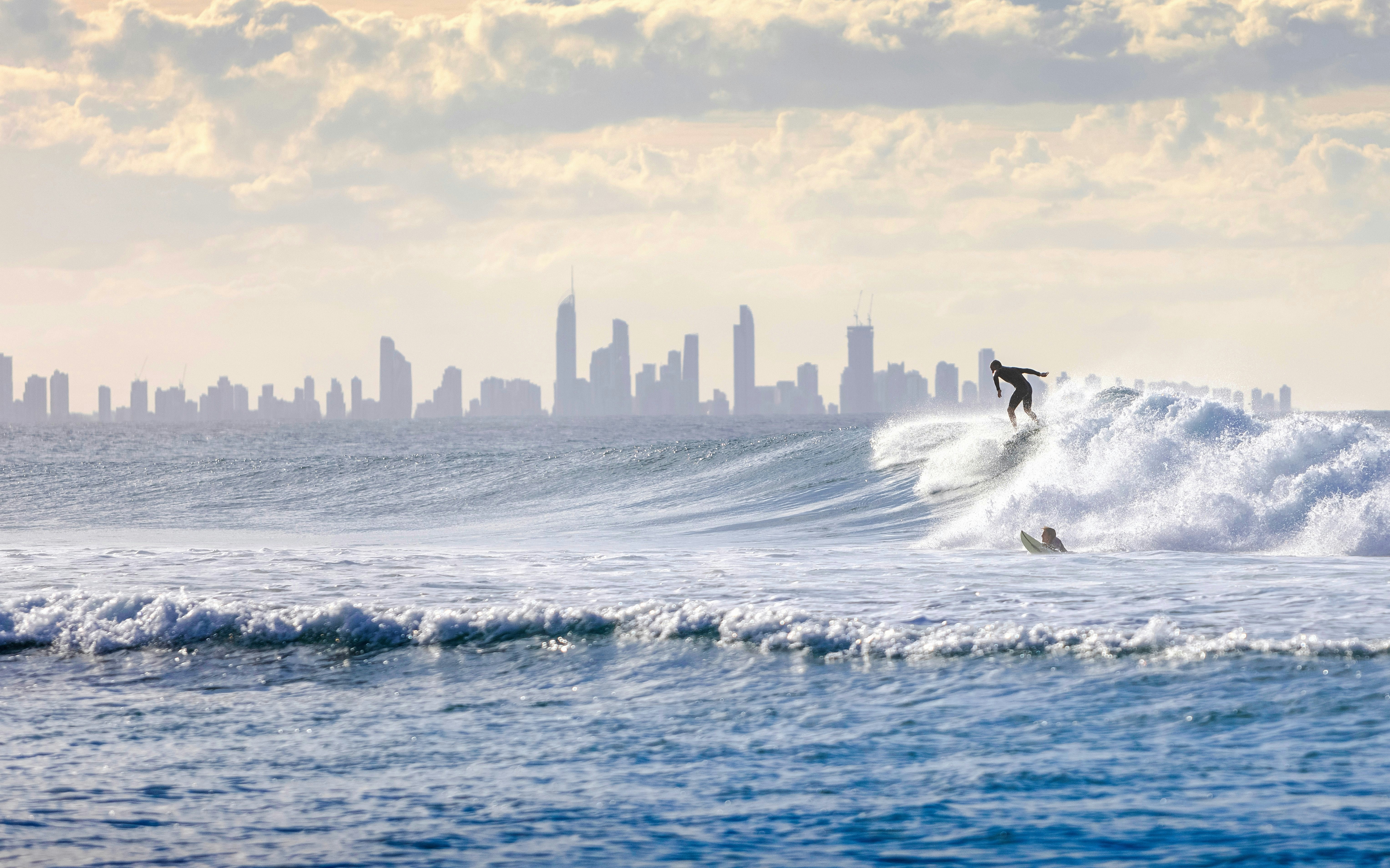 surfisti che cavalcano le onde al largo di Surfers Paradise con lo skyline della Gold Coast sullo sfondo