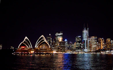 Sydney Opera House and city skyline at night with reflections on the water.