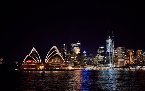Sydney Opera House and city skyline at night with reflections on the water.