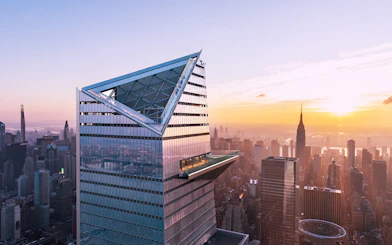Visitors on Edge Observation Deck with New York City skyline at sunset.