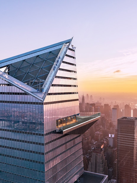 Visitors on Edge Observation Deck with New York City skyline at sunset.