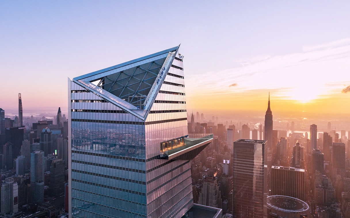 Visitors on Edge Observation Deck with New York City skyline at sunset.