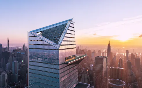 Visitors on Edge Observation Deck with New York City skyline at sunset.