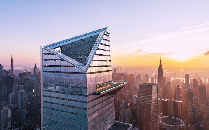 Visitors on Edge Observation Deck with New York City skyline at sunset.