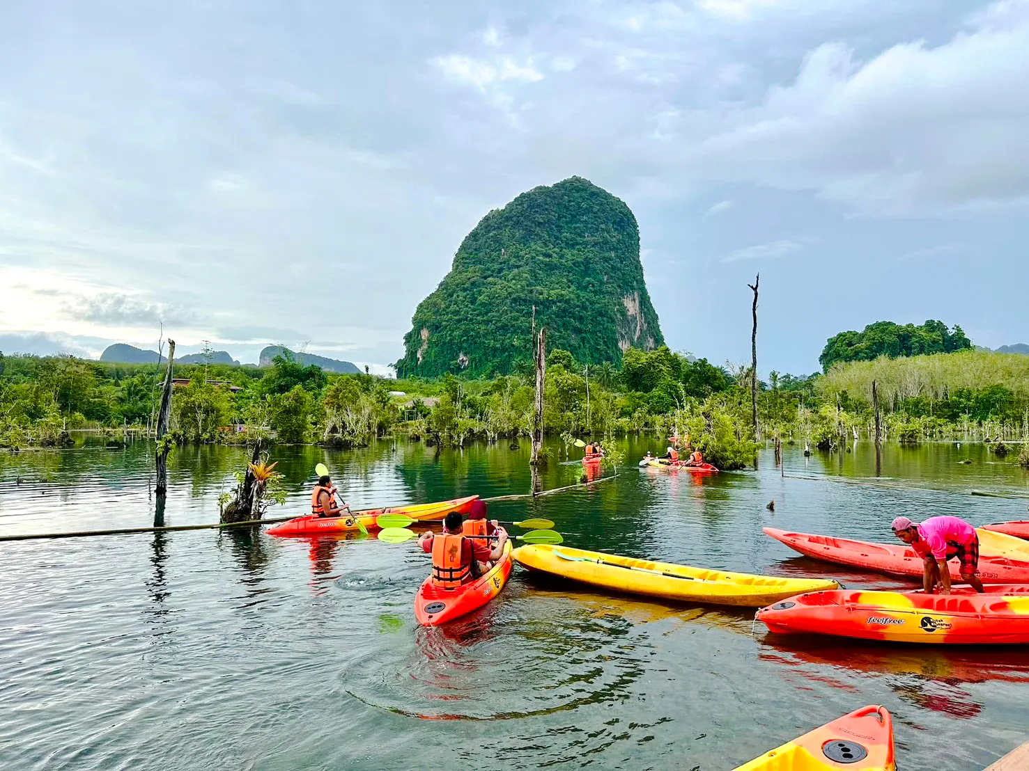 Kayakers paddling in a scenic Krabi lagoon with a lush limestone hill in the background.