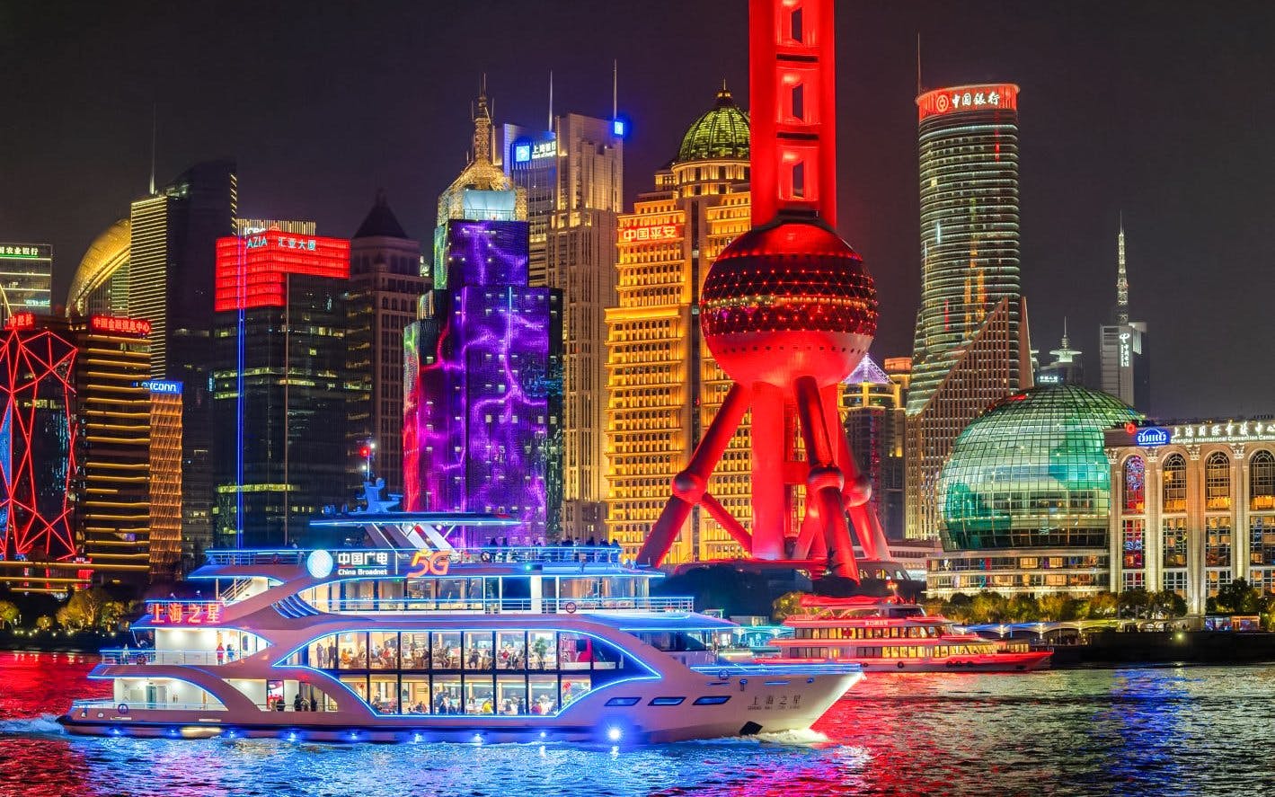Boat cruising on the Huangpu River with Shanghai skyline and Oriental Pearl Tower illuminated at night.