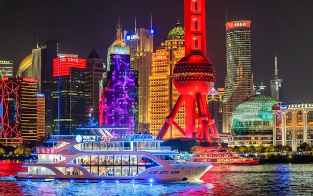 Boat cruising on the Huangpu River with Shanghai skyline and Oriental Pearl Tower illuminated at night.