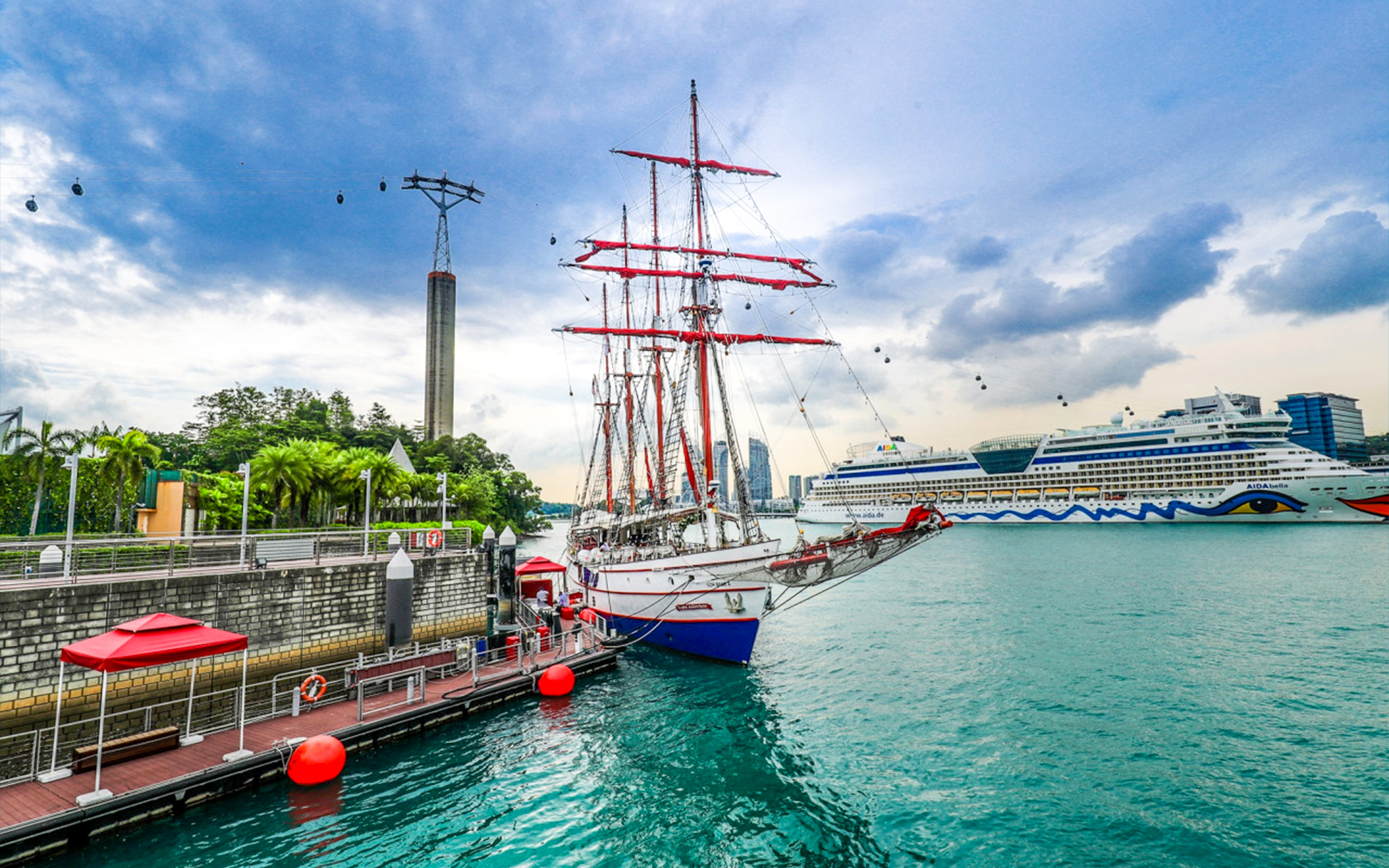 Tall ship docked at Singapore harbor with cable cars and cruise ship in the background.