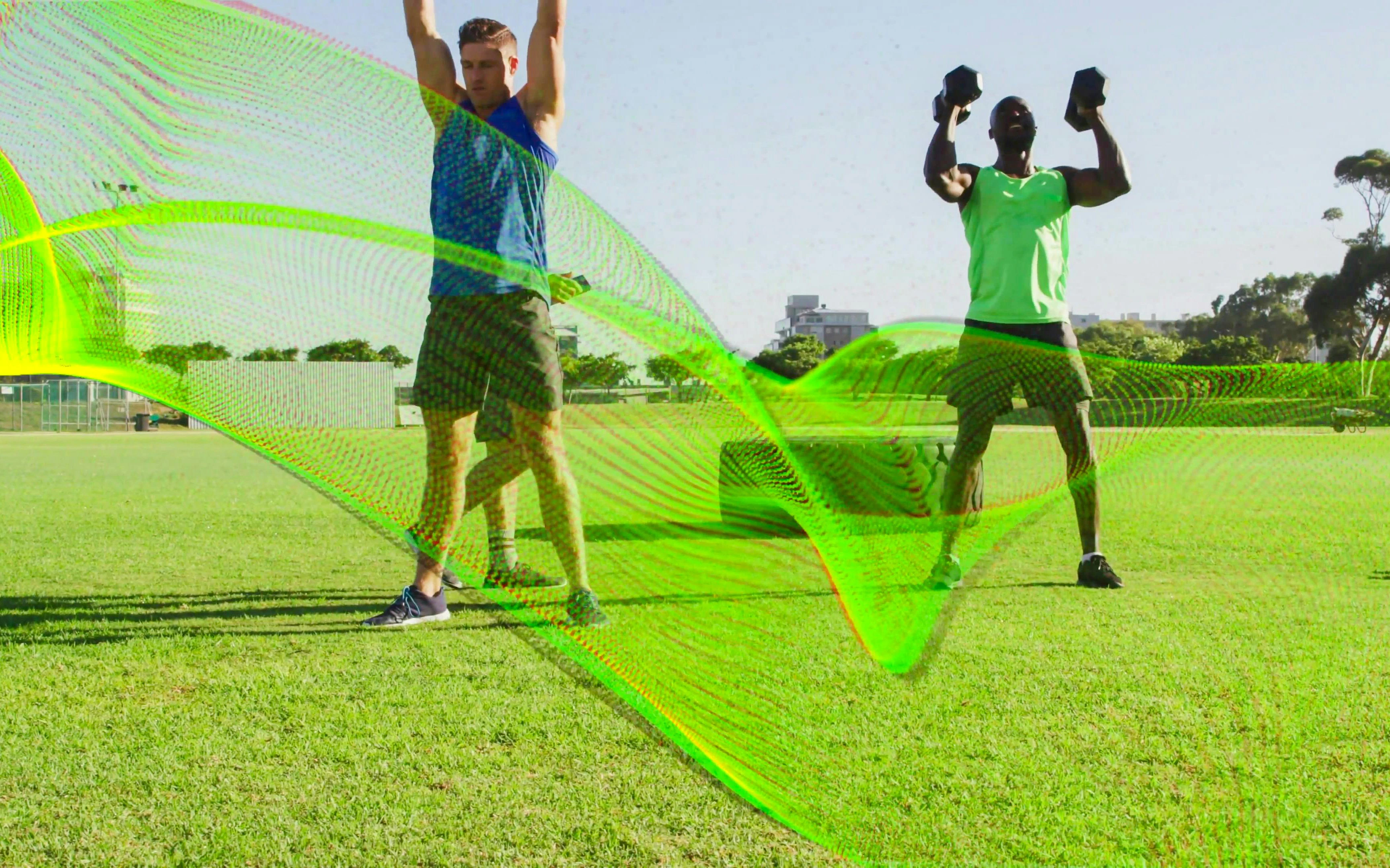 Three men lifting dumbbells on a sports field with a neon mesh and tractor tire in the background.