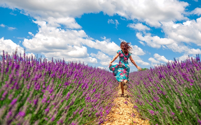 Woman running through a lavender field under a blue sky.