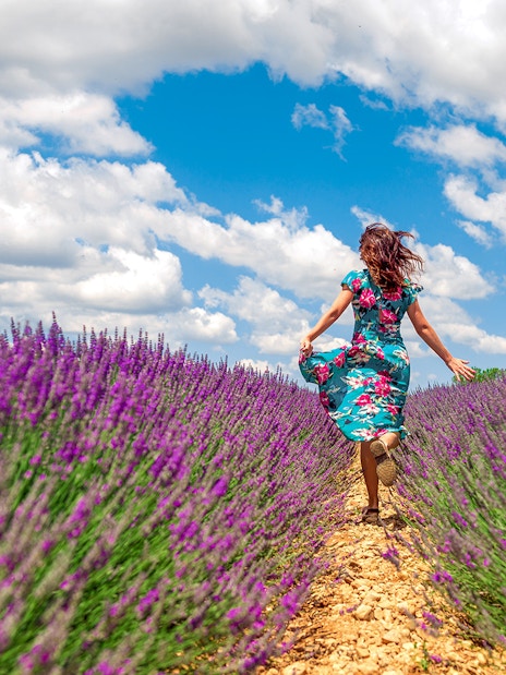 Woman running through a lavender field under a blue sky.