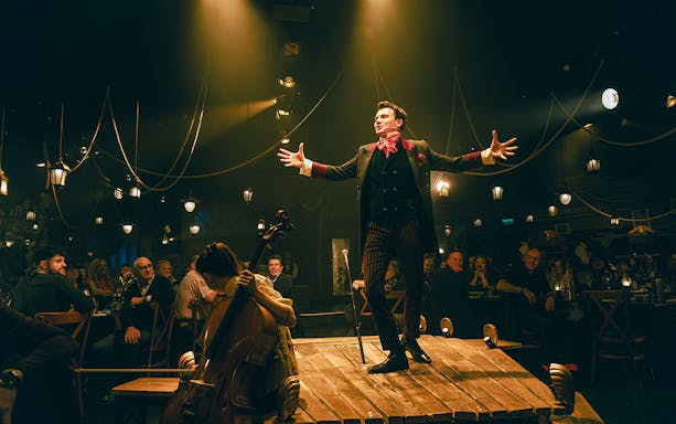 Performer on stage during The Great Christmas Feast with audience and cellist.