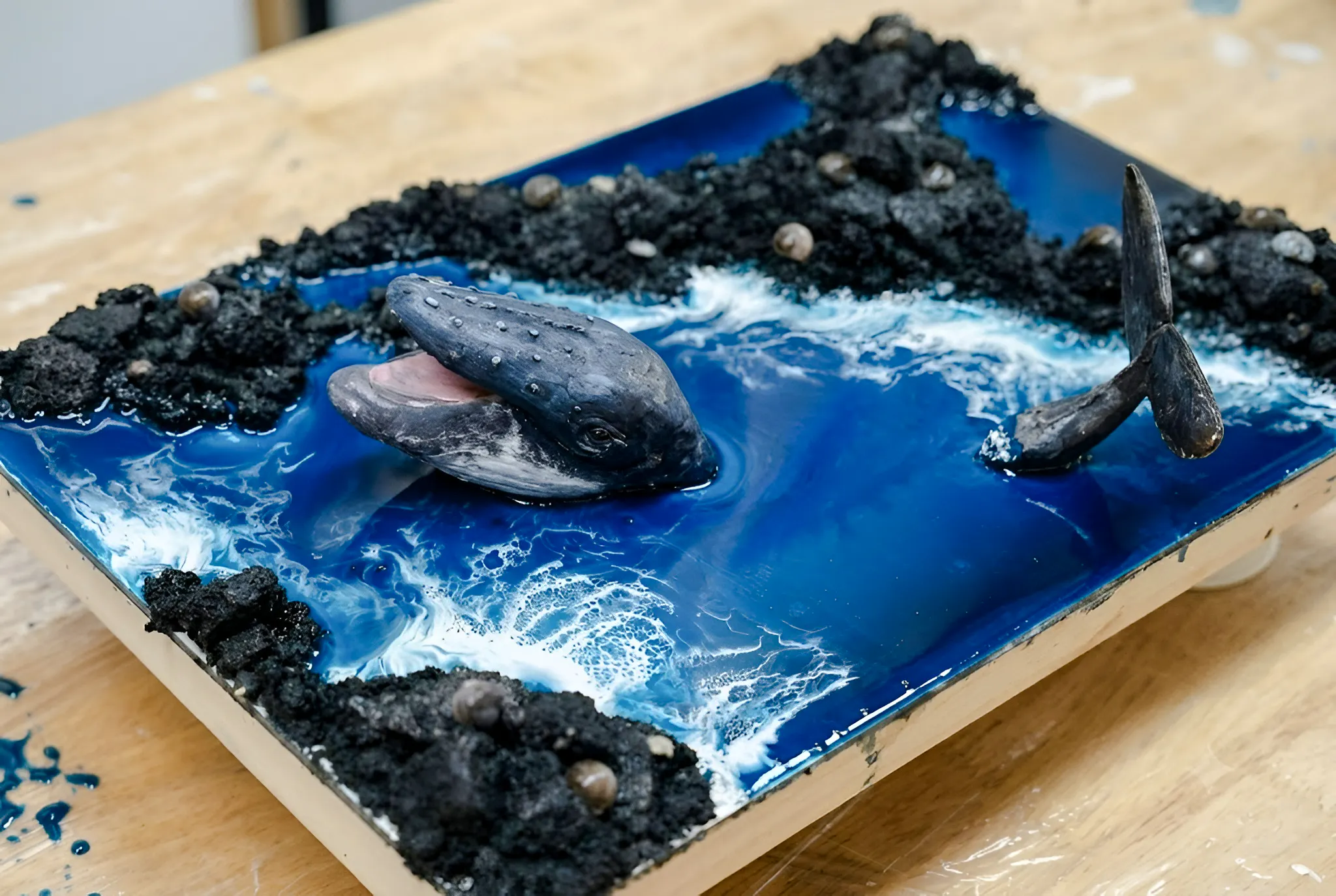 Whale sculpture emerging from ocean-themed artwork in Hanoi workshop.