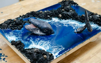 Whale sculpture emerging from ocean-themed artwork in Hanoi workshop.