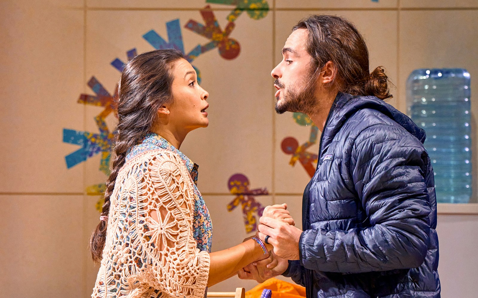 Two actors in a dramatic scene from the play "Eureka Day," holding hands and speaking intensely.