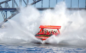Jet boat splashing through water near Sydney Harbour Bridge with passengers.