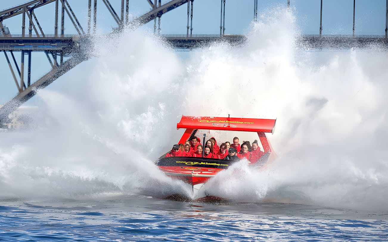 Jet boat splashing through water near Sydney Harbour Bridge with passengers.