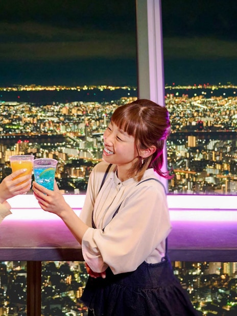 Tourists toasting drinks at TOKYO SKYTREE Tembo Deck with city lights view.