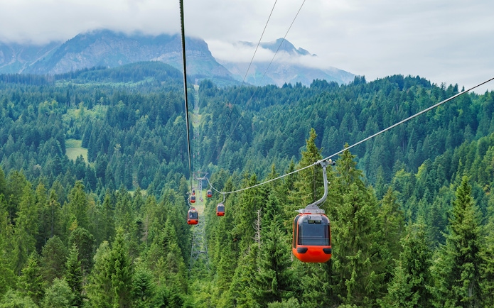 Pilatus Kulm cable cars ascending over lush green forest with mountains in the background.
