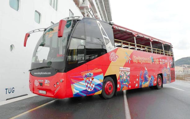 Open-top red tour bus in Split, Croatia, parked near a cruise ship.