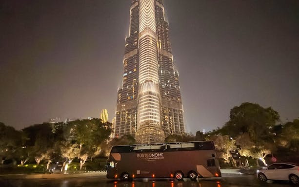 Bustronome restaurant bus parked near Burj Khalifa in Dubai at night.