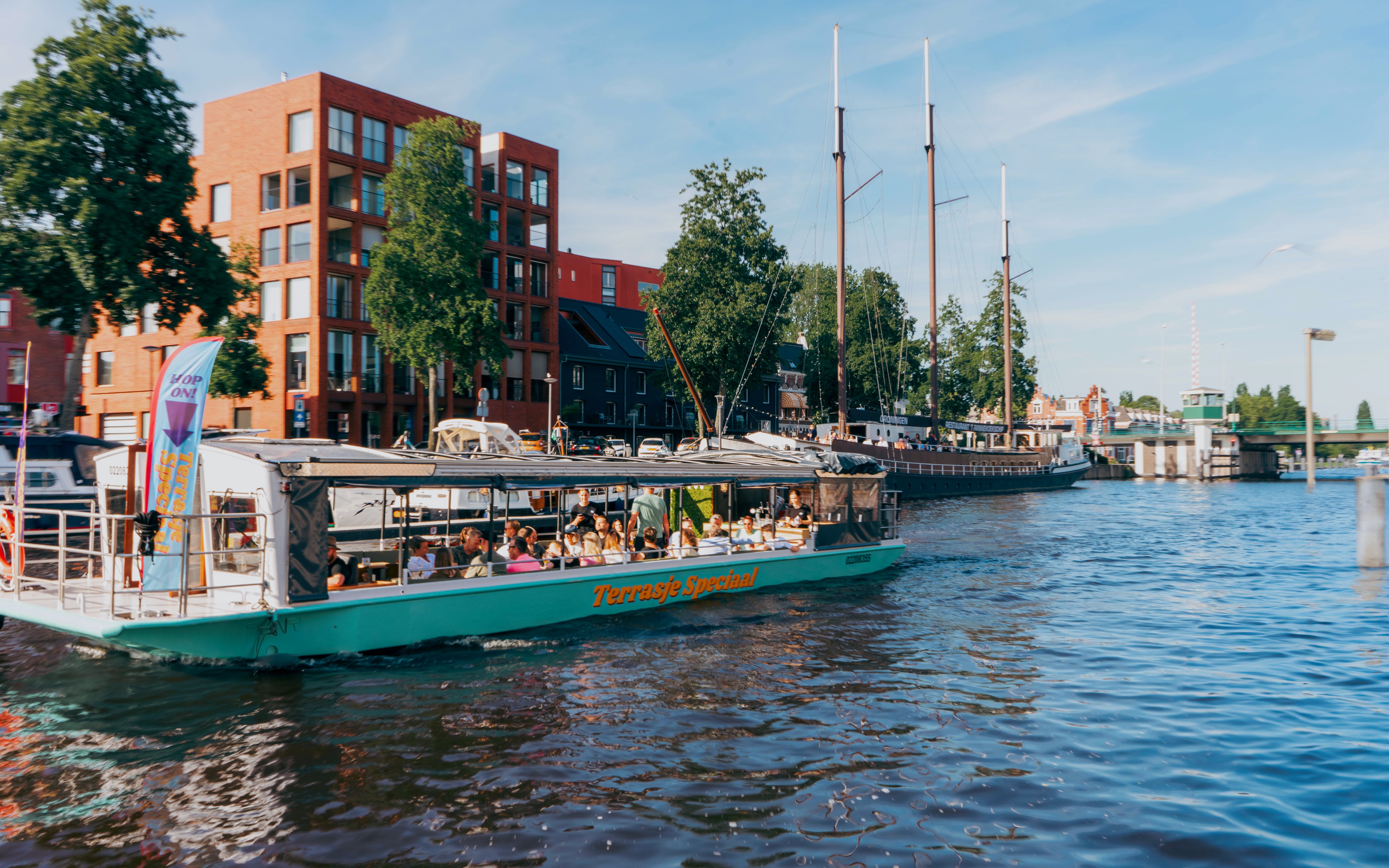 Terrace boat with passengers cruising a canal in Groningen, passing by modern buildings.