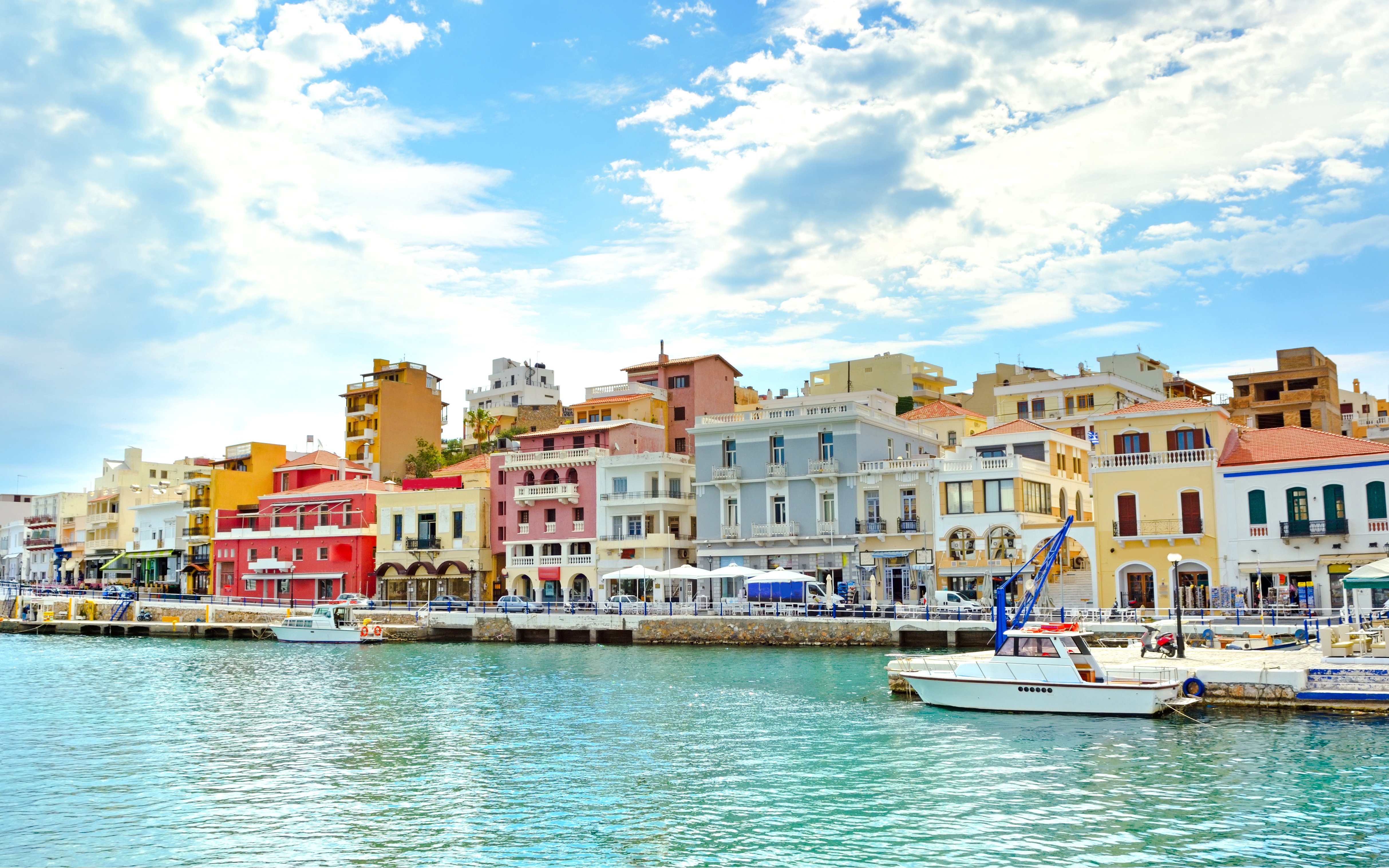 Colorful waterfront buildings in Agios Nikolaos, Corfu, Greece, with a boat docked in the foreground.