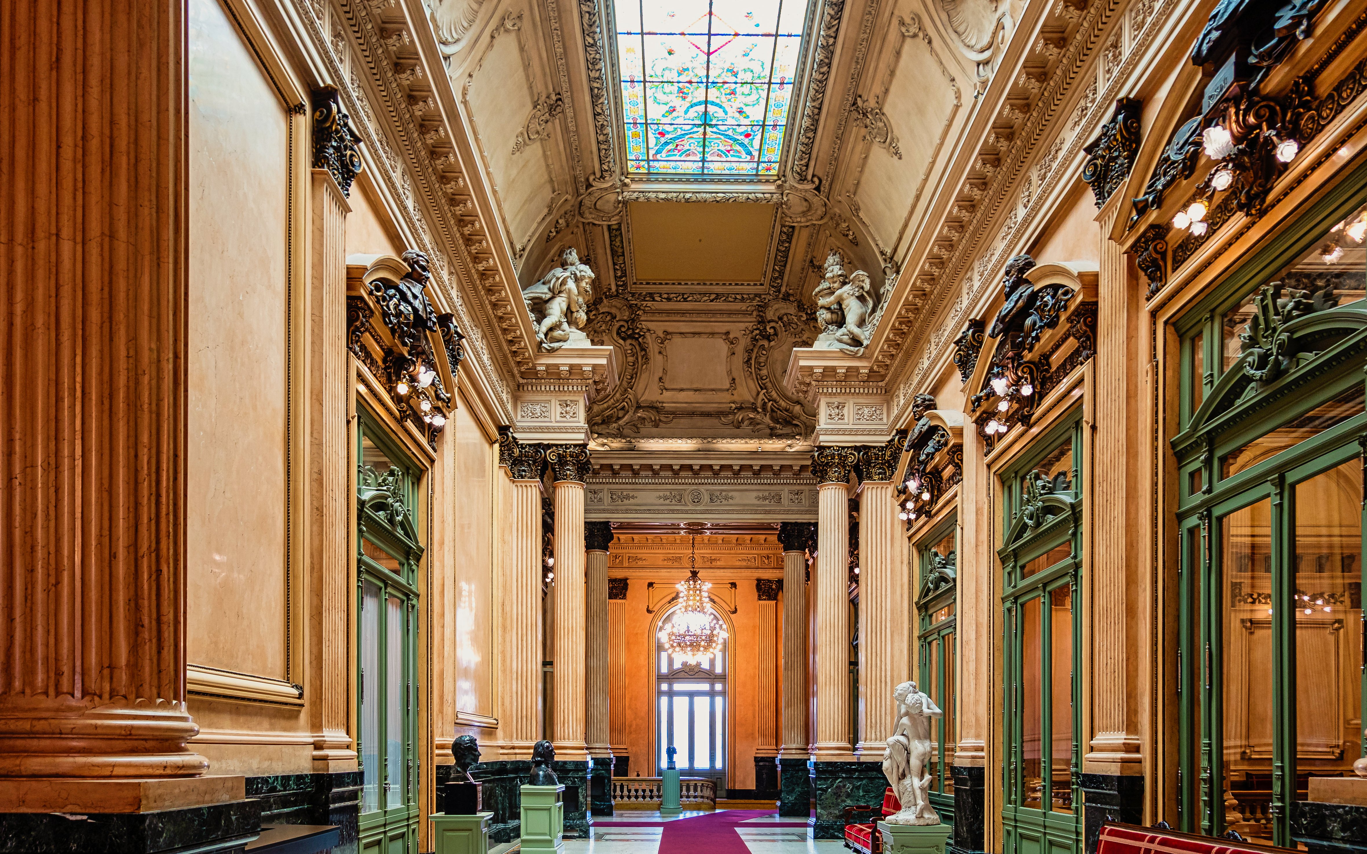 Teatro Colon interior with ornate columns, statues, and stained glass ceiling.