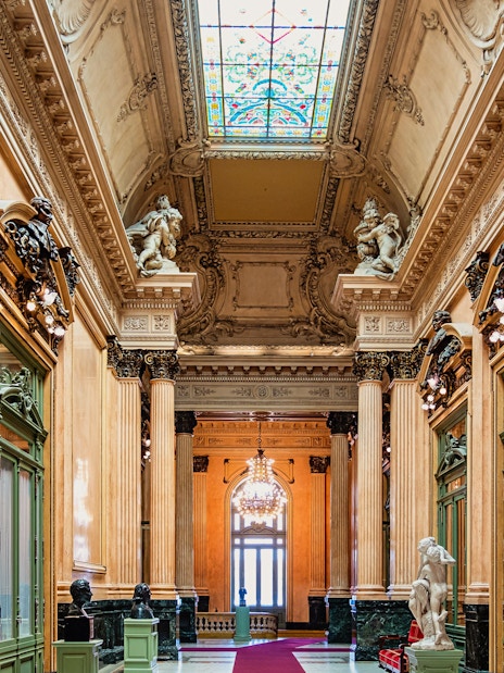 Teatro Colon interior with ornate columns, statues, and stained glass ceiling.