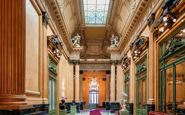 Teatro Colon interior with ornate columns, statues, and stained glass ceiling.