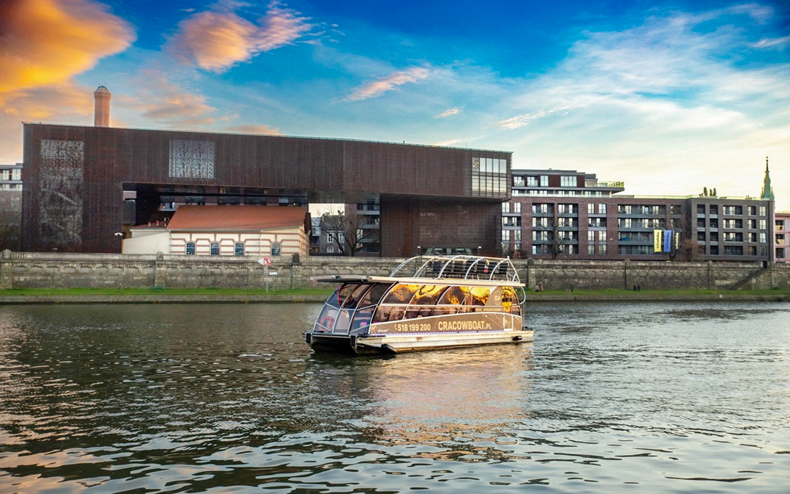 Cruise boat on Vistula River with modern buildings in Krakow, Poland.