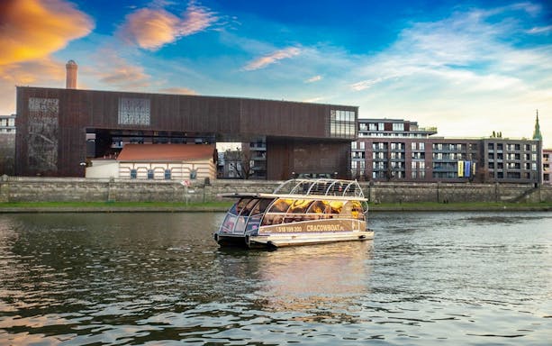 Cruise boat on Vistula River with modern buildings in Krakow, Poland.