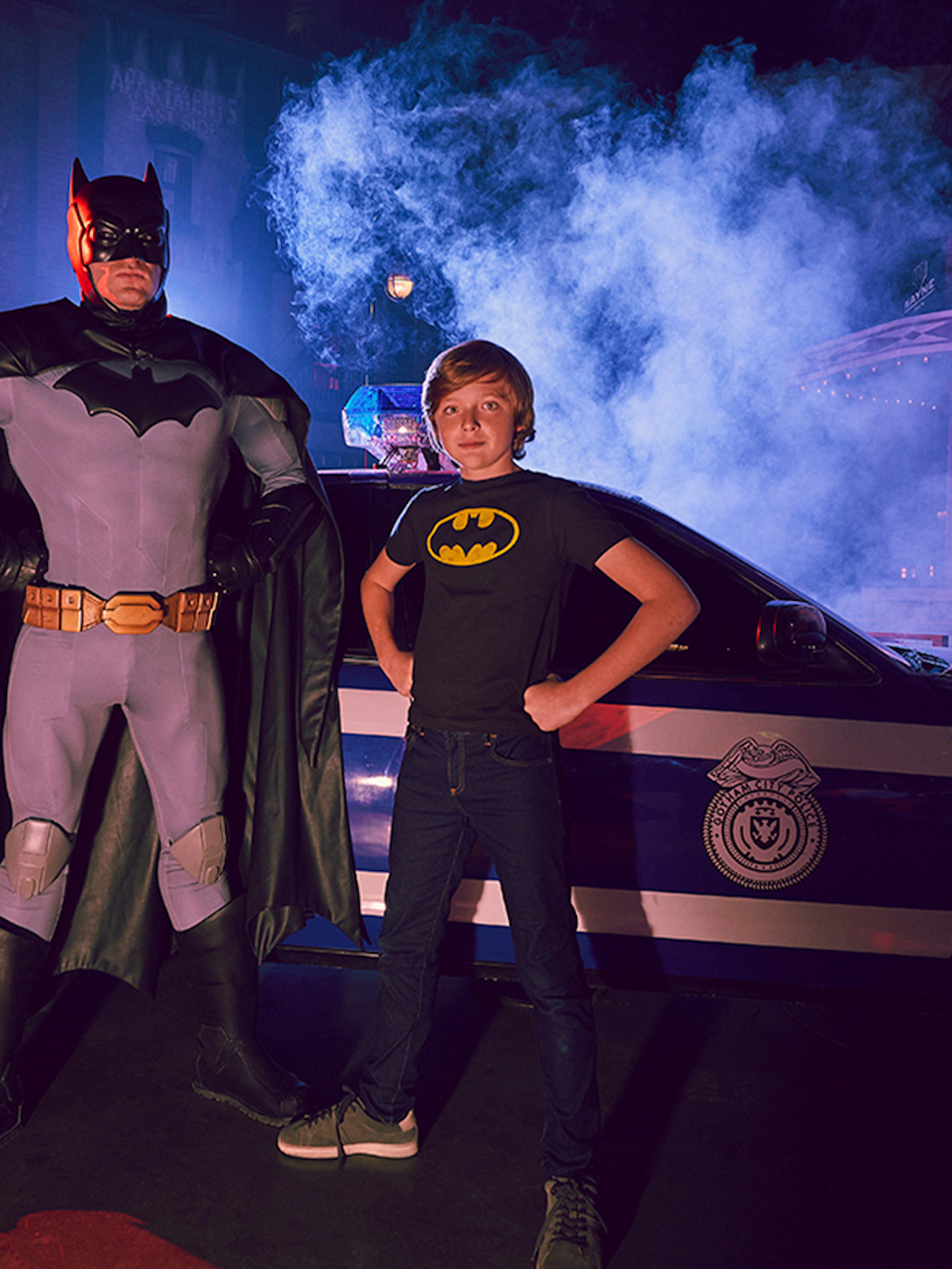 Batman character and child pose in front of police car at Warner Bros. World Abu Dhabi.