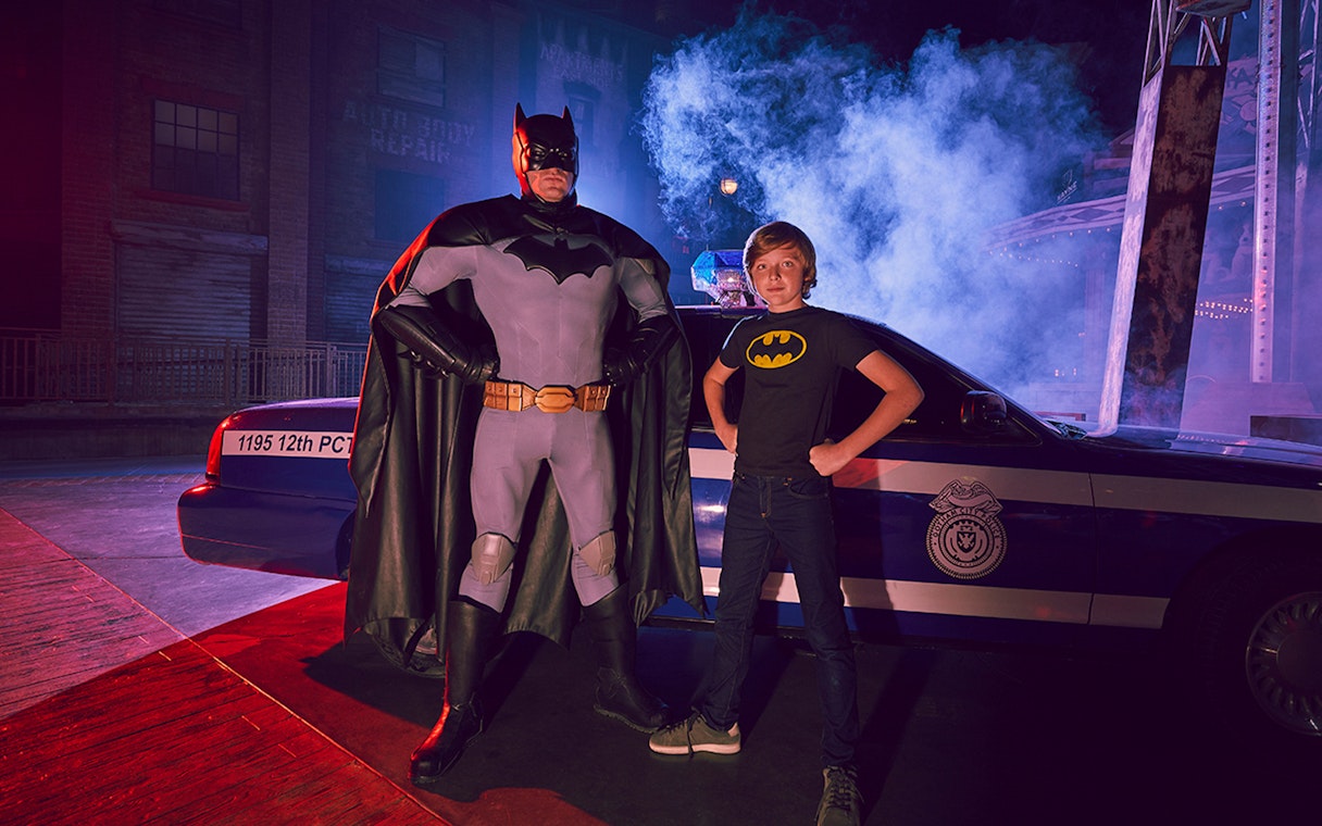 Batman character and child pose in front of police car at Warner Bros. World Abu Dhabi.