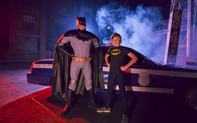 Batman character and child pose in front of police car at Warner Bros. World Abu Dhabi.