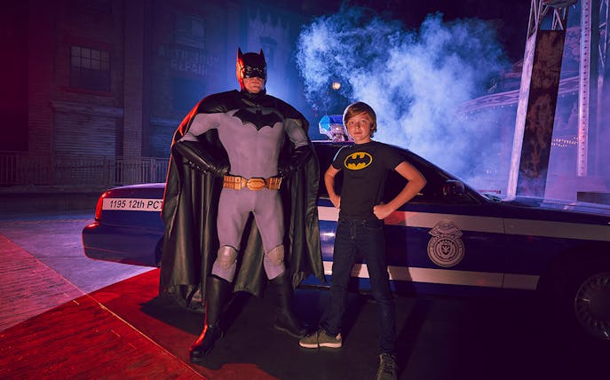 Batman character and child pose in front of police car at Warner Bros. World Abu Dhabi.