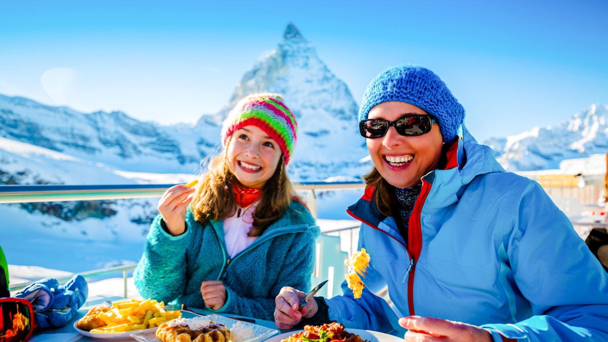 Tourists enjoying Swiss fondue dinner with Matterhorn view in Switzerland.