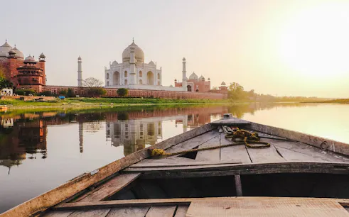 Boat view of the Taj Mahal and riverbank during sunset on Agra heritage tour.
