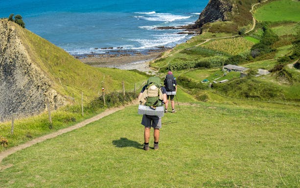 Hikers on St James Way trail from San Sebastian to San Pedro with coastal view.
