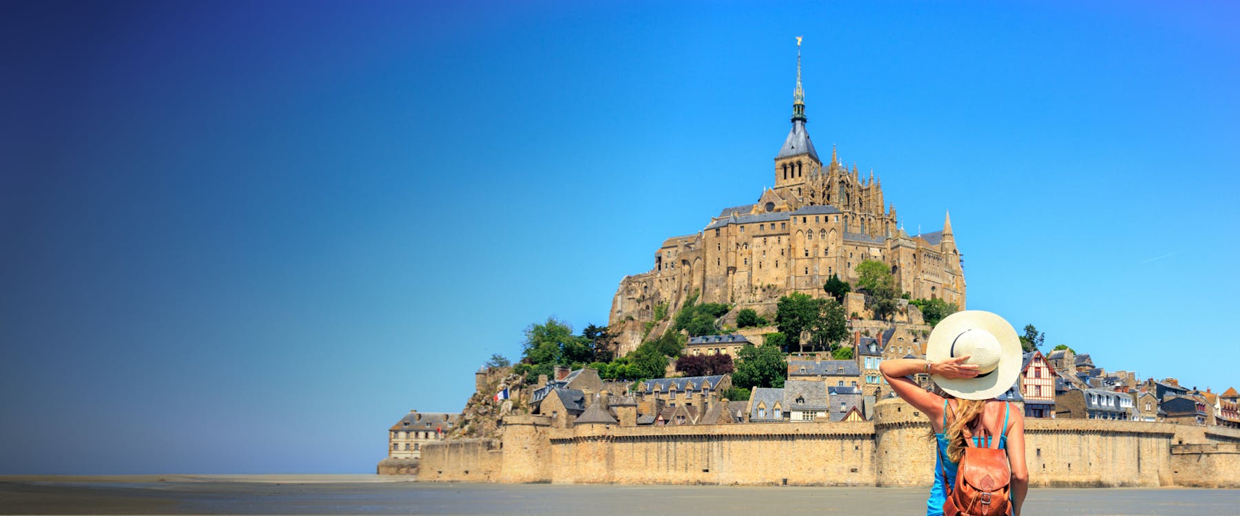 Traveler admiring Mont Saint Michel in France with clear blue sky.