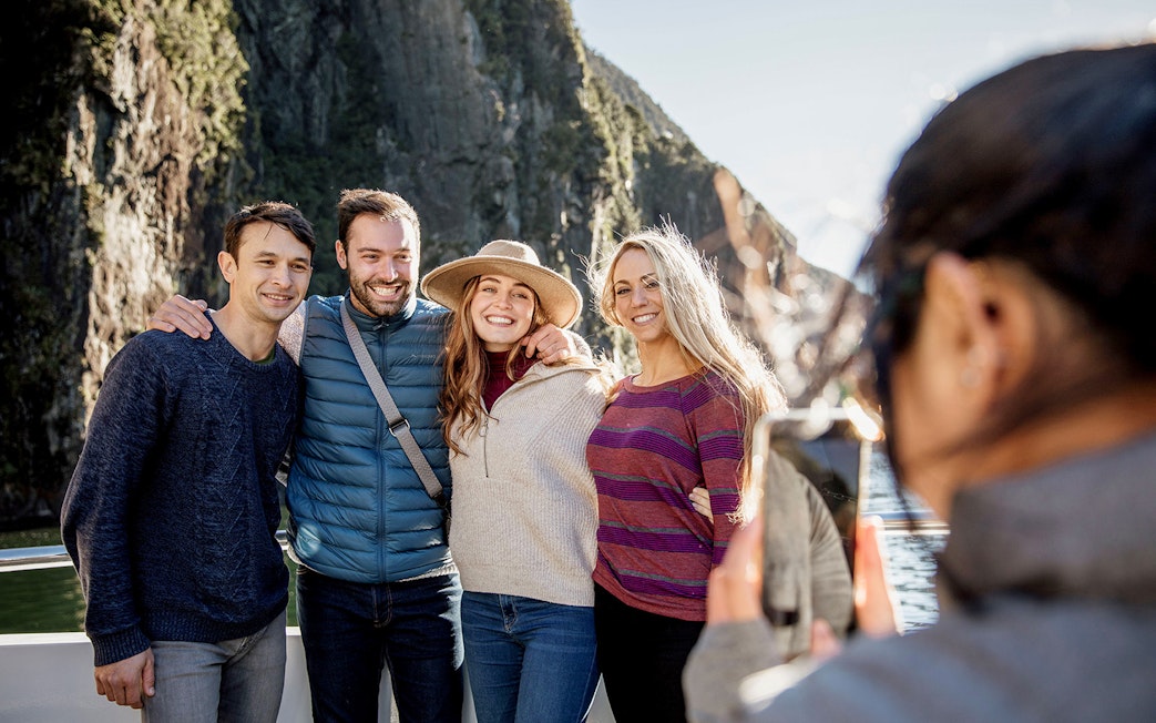 Group posing on Milford Sound cruise with cliffs in background, Queenstown day trip.
