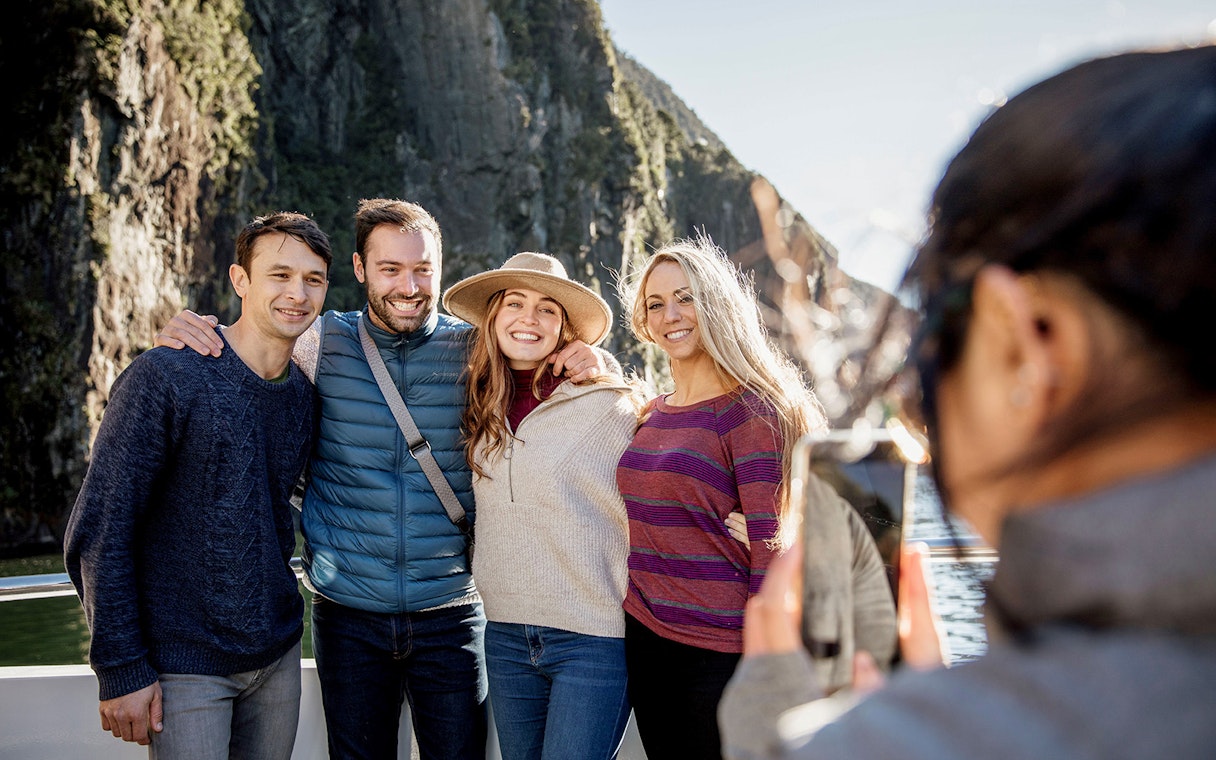 Group posing on Milford Sound cruise with cliffs in background, Queenstown day trip.