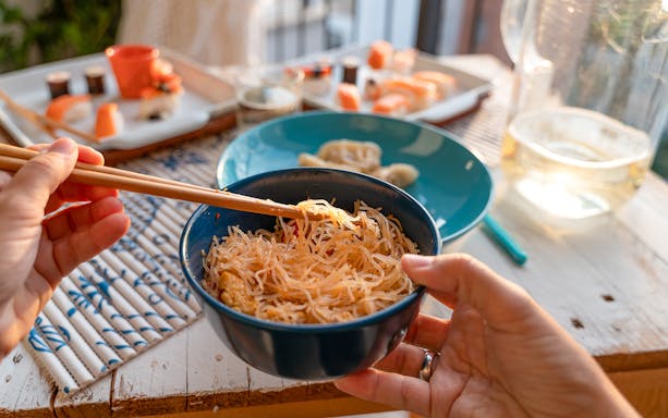 Chopsticks holding noodles with sushi and dumplings on a table during Tokyo tour.