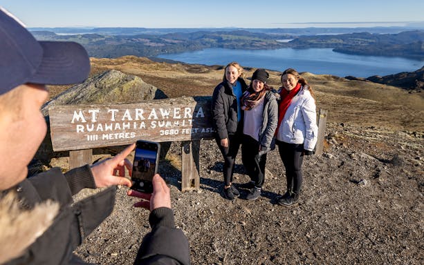 Visitors posing at Mount Tarawera summit with scenic view during guided volcanic walk.