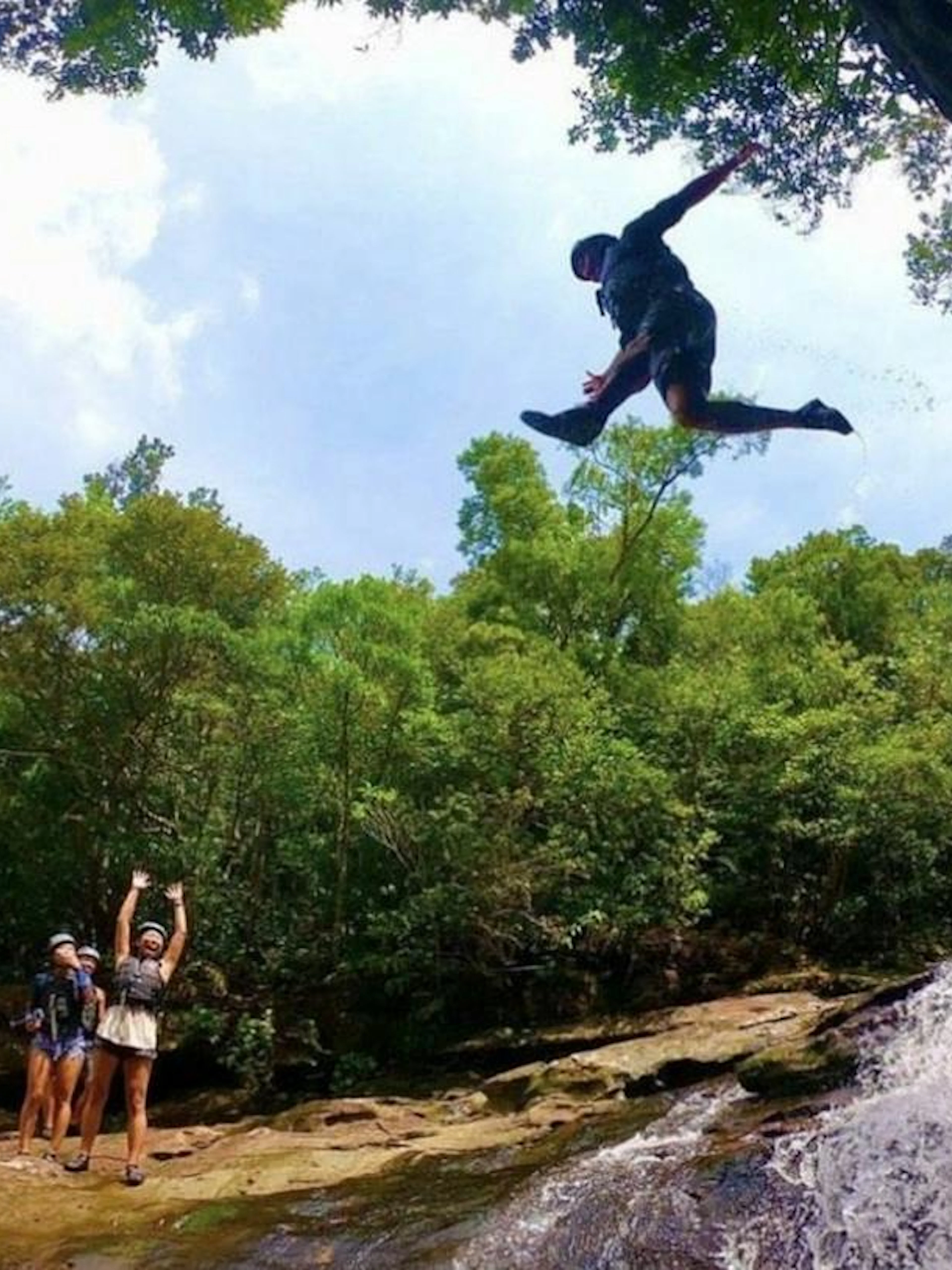 Canyoning adventure in Iriomote, Okinawa with a person jumping near a waterfall.