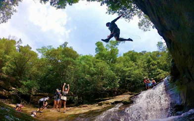 Canyoning adventure in Iriomote, Okinawa with a person jumping near a waterfall.