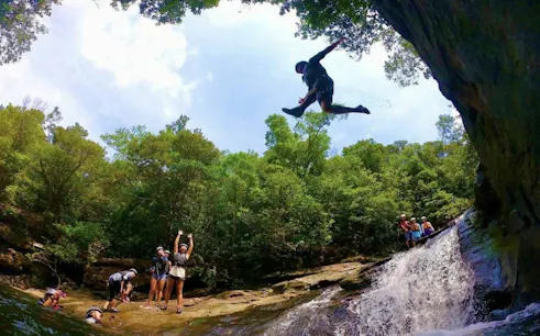 Canyoning adventure in Iriomote, Okinawa with a person jumping near a waterfall.