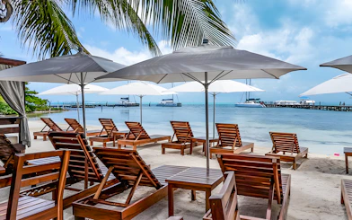 Beachfront lounge chairs under umbrellas with catamarans docked at Isla Mujeres.