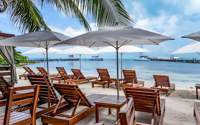 Beachfront lounge chairs under umbrellas with catamarans docked at Isla Mujeres.